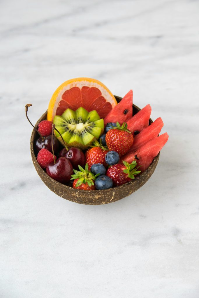 a bowl of grapefruit, kiwi, strawberries and blueberries on a grey and white marble countertop