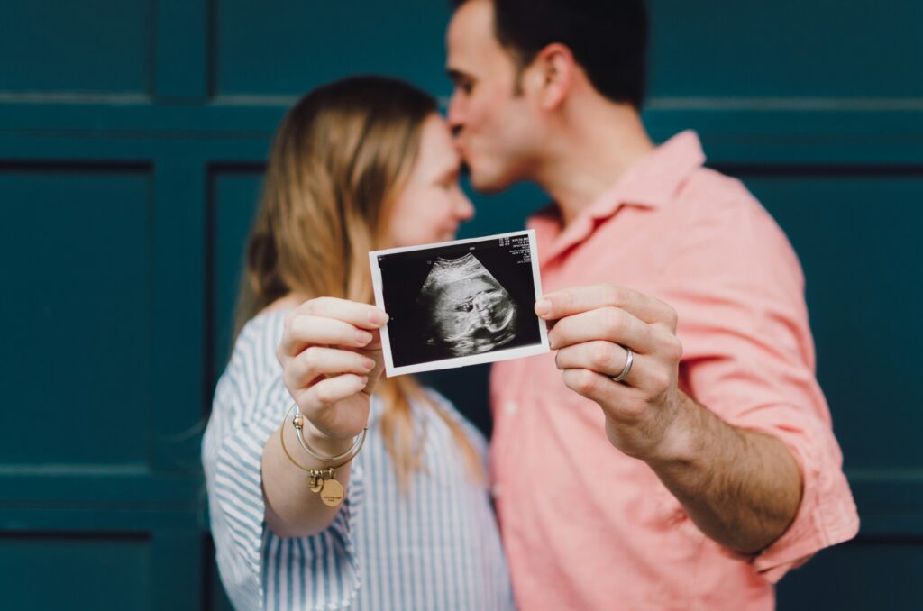 couple kissing while holding up a sonogram picture