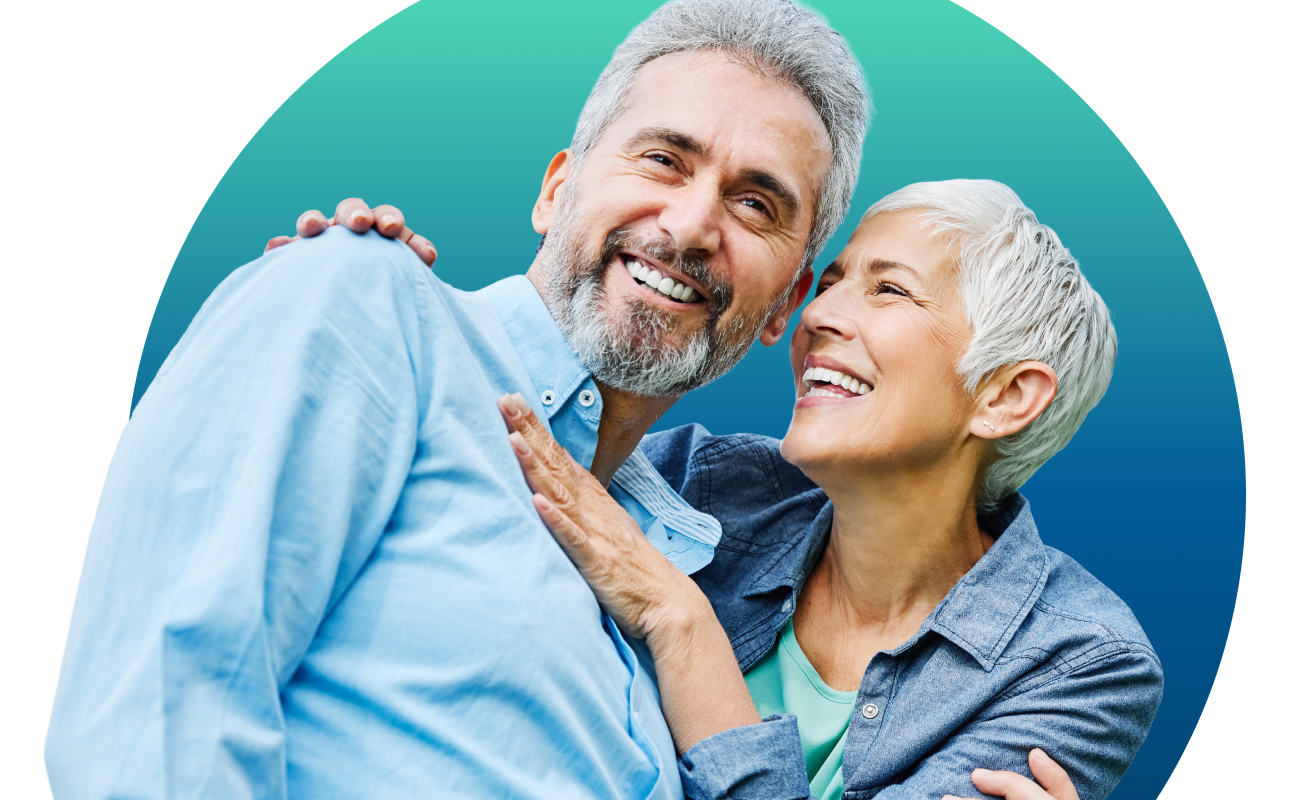A happy senior couple smiling and laughing together against a teal and blue circular gradient background. The man, with grey hair and a beard, is wearing a light blue button-down shirt, while the woman, with short silver hair, leans against him in a denim shirt.