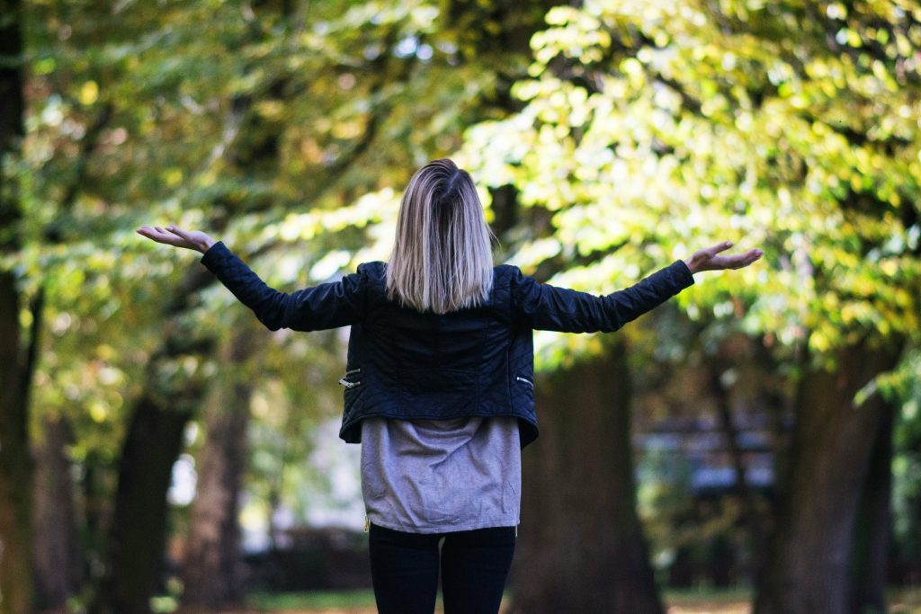 image of the back of a woman spreading out her arms in wonder while facing trees