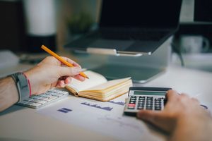 Hands holding a pencil and calculator, writing in a notebook
